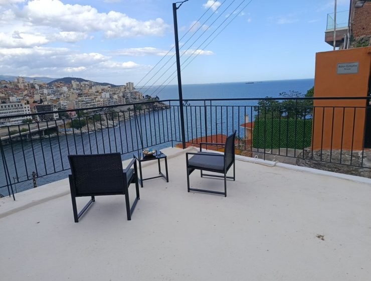 Terrace seating with two black chairs and a small table overlooking a coastal town and blue sea.