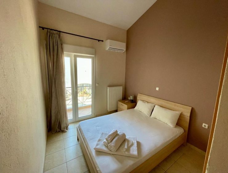 Bedroom with a double bed, two pillows, folded towels on the sheets, and a balcony door to outdoors. (informative)