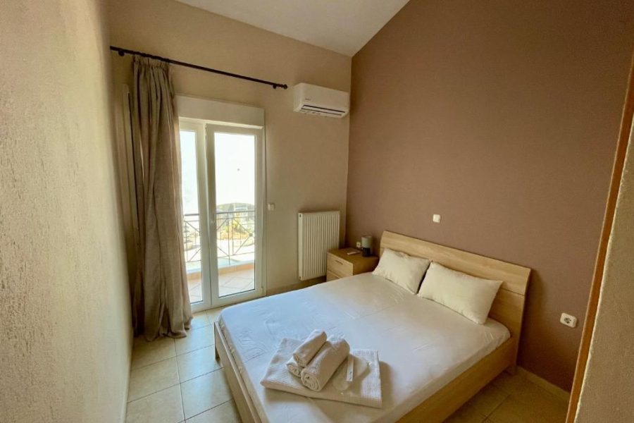 Bedroom with a double bed, two pillows, folded towels on the sheets, and a balcony door to outdoors. (informative)